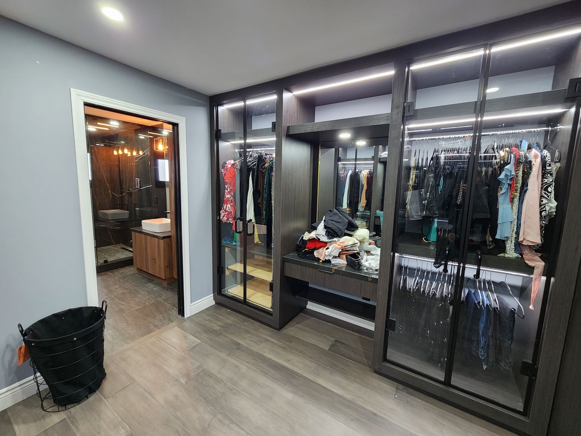 A walk in closet with lots of clothes in it and a bathroom in the background.