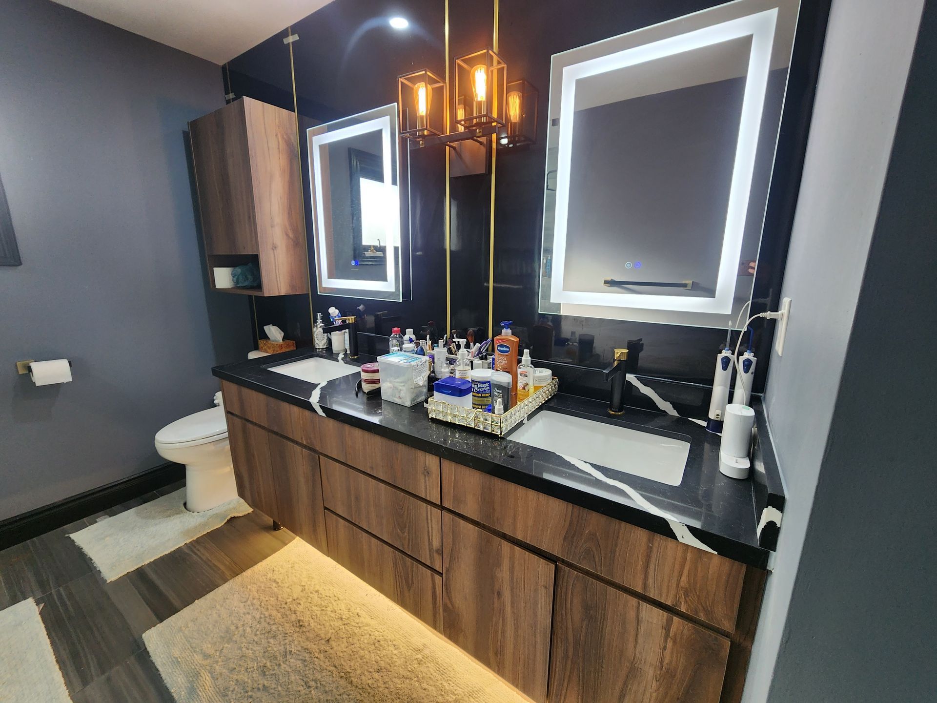 A bathroom with two sinks , two mirrors and a toilet.