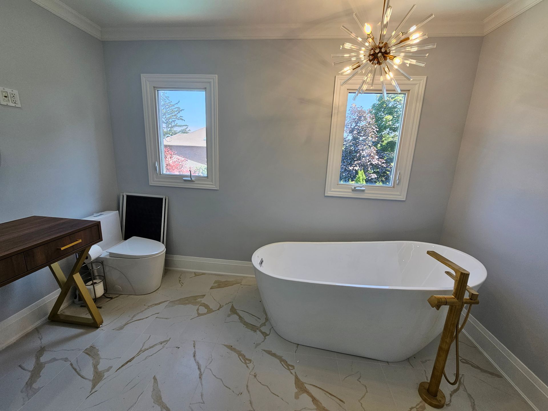 A bathroom with a bathtub , toilet , desk and window.