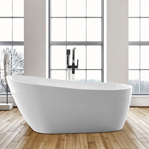 A white bathtub is sitting on a wooden floor in a bathroom next to a window.