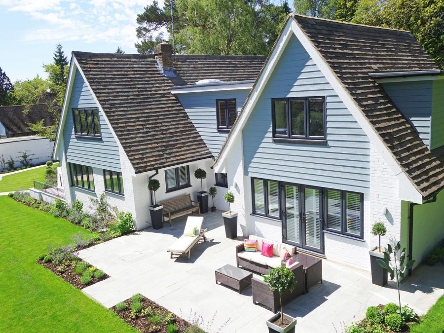 House with blue siding, brown roof, patio with furniture and green lawn.