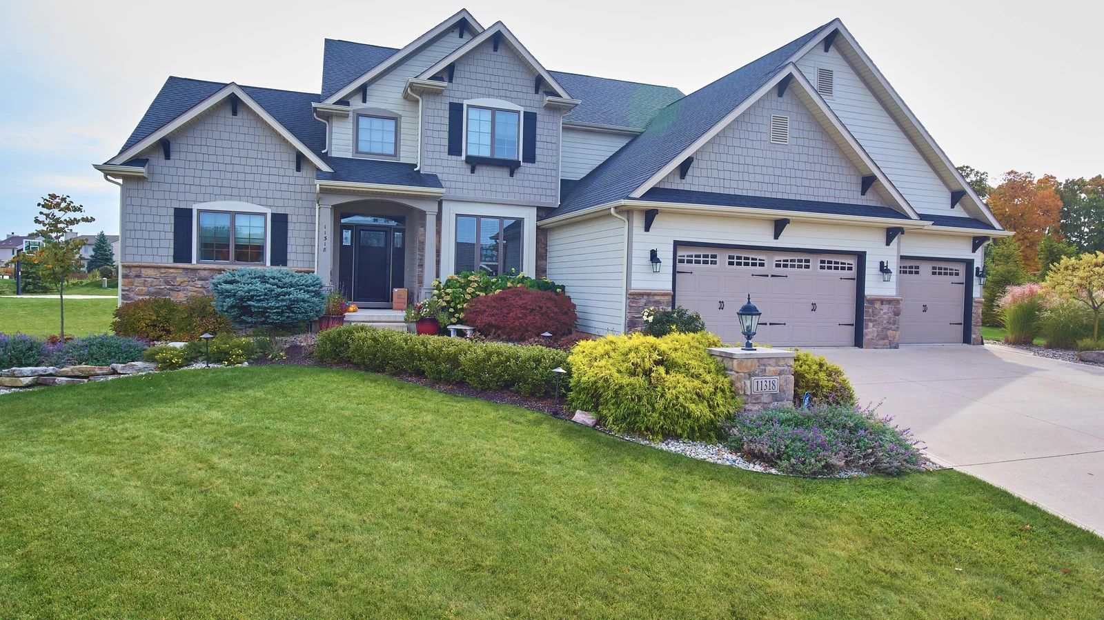Two-story house with gray brick facade, green lawn, and beige garage doors.