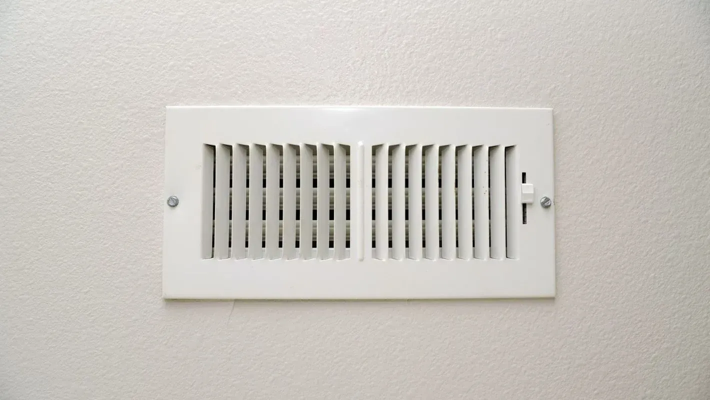 White rectangular air vent on a white wall, two screws visible.