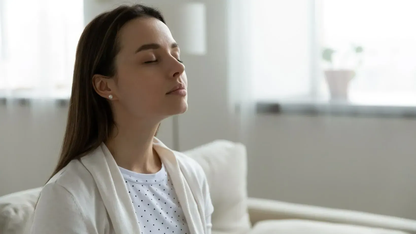 Woman with eyes closed, sitting indoors, taking a deep breath.