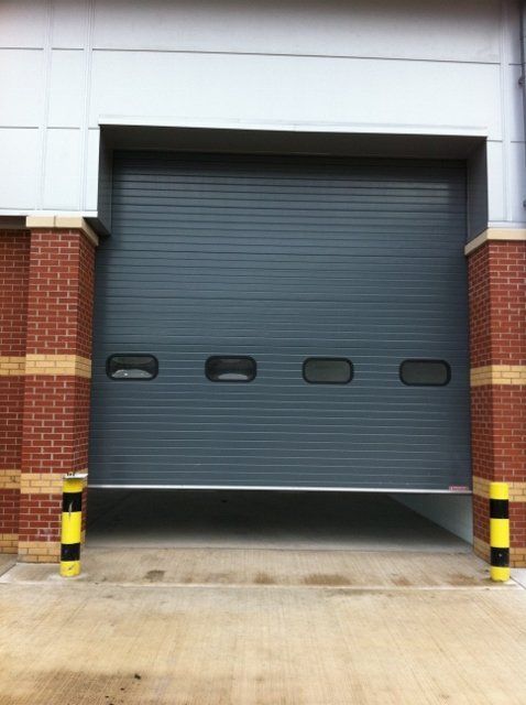 A grey garage door with a brick wall behind it