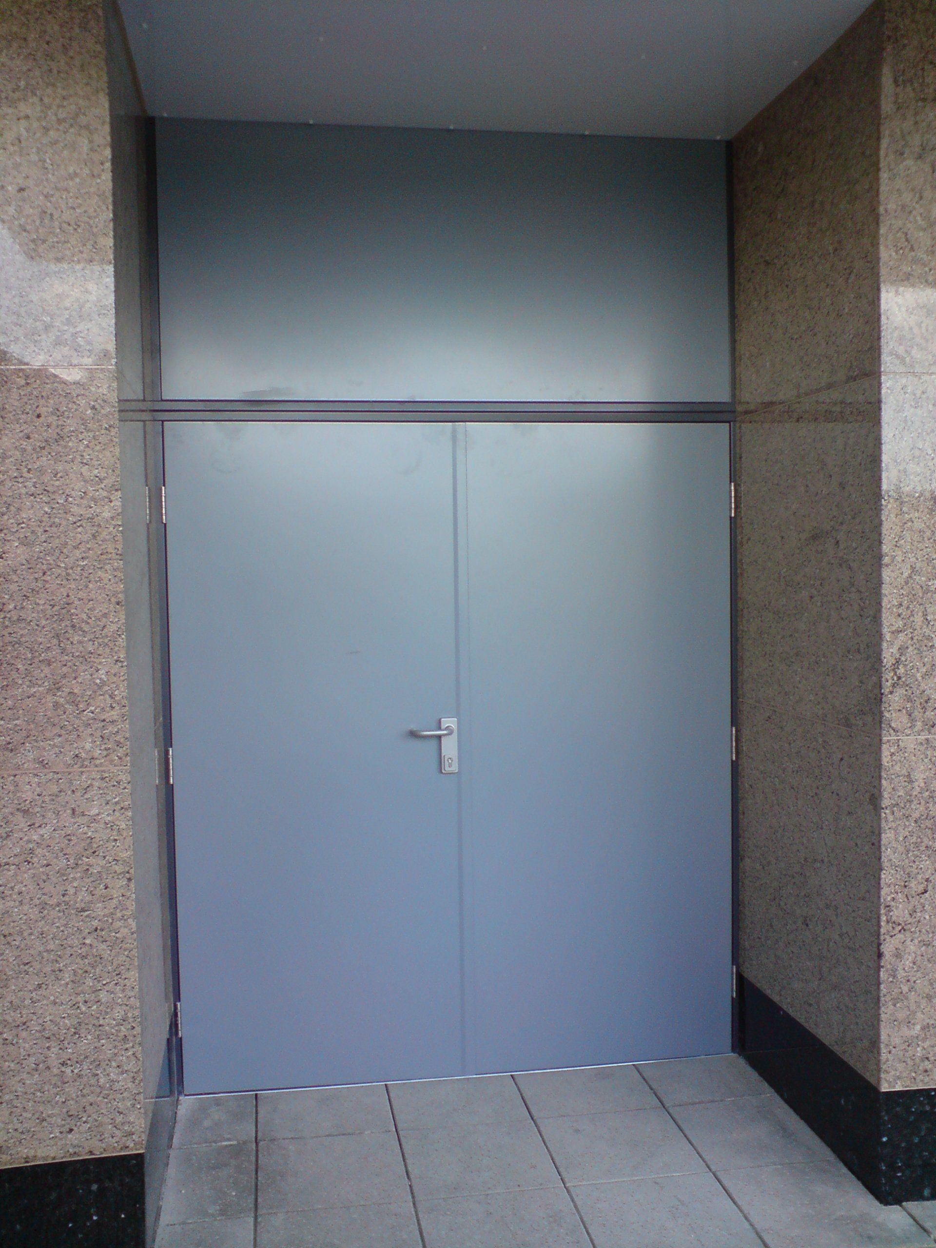 A large grey door is between two granite walls