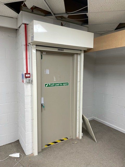 An empty room with a door and a fire alarm on the wall.