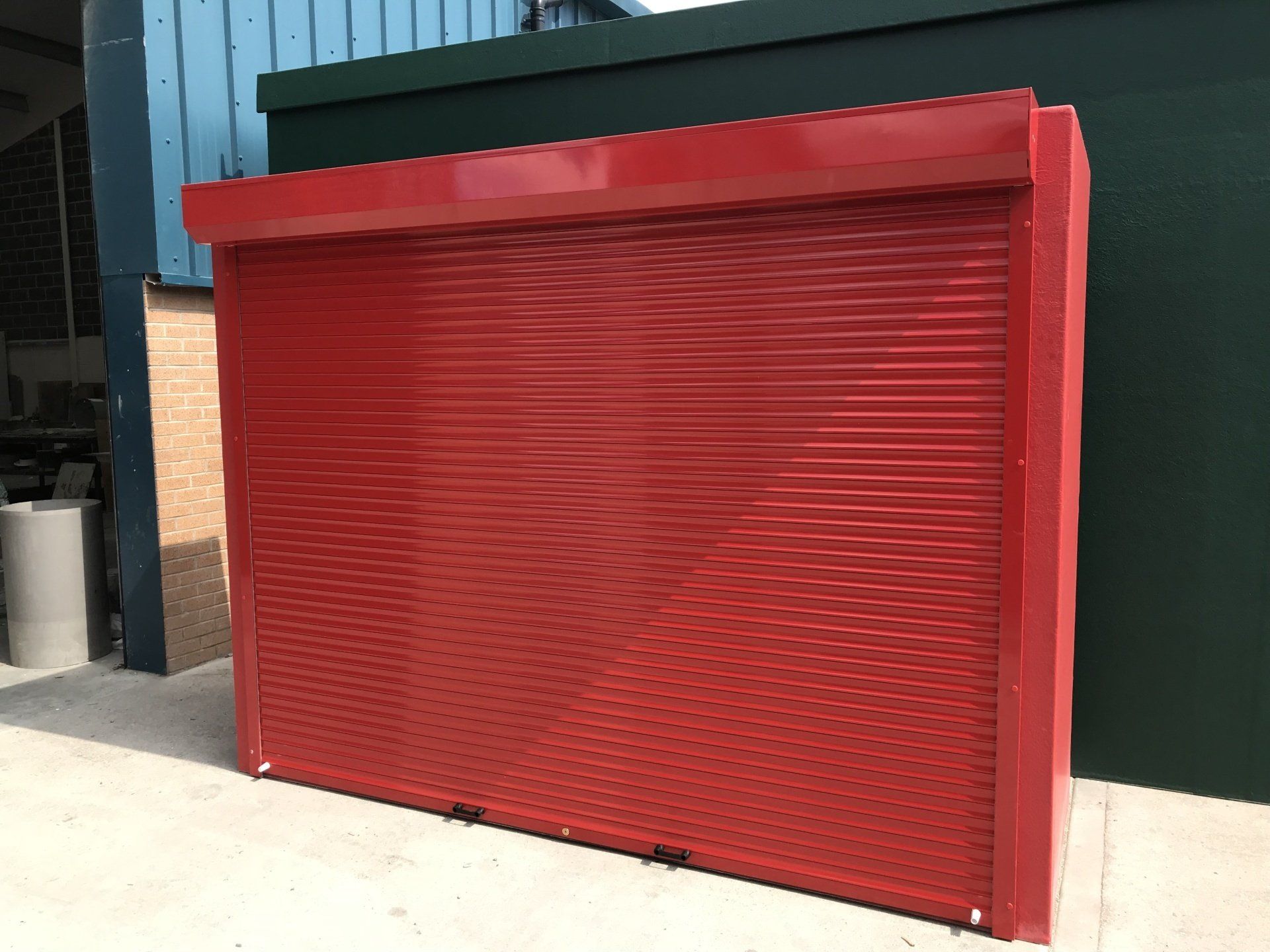 A red garage door is sitting in front of a green building.