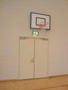 A basketball hoop is hanging on the wall above a door in a gym.