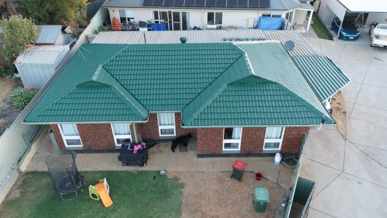 Aerial view of a brick house with a green roof, backyard, and driveway area.