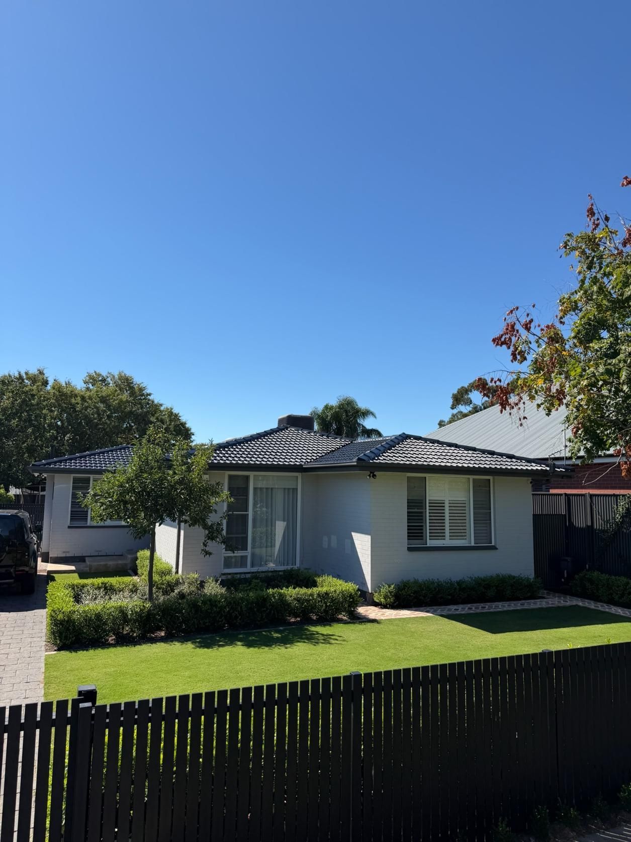 Single-story white house with dark roof, green lawn, and a black fence under a clear blue sky.
