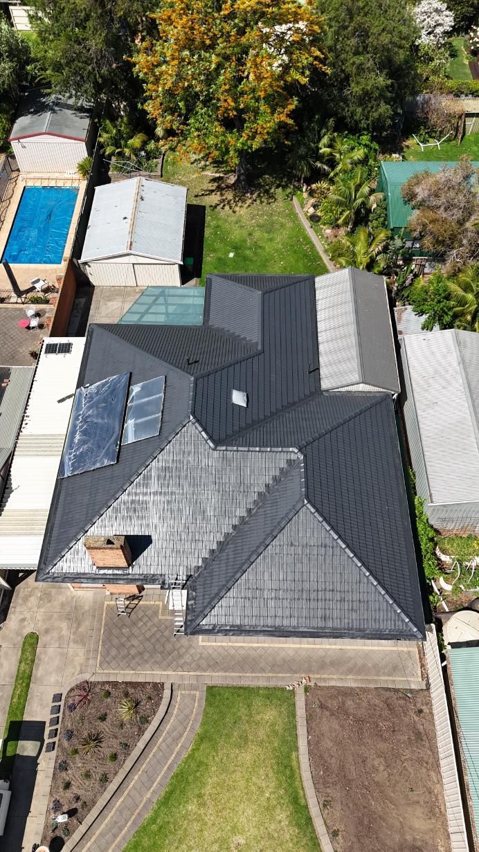 Aerial view of a house with a dark gray roof, front lawn, and surrounding trees and neighboring yards