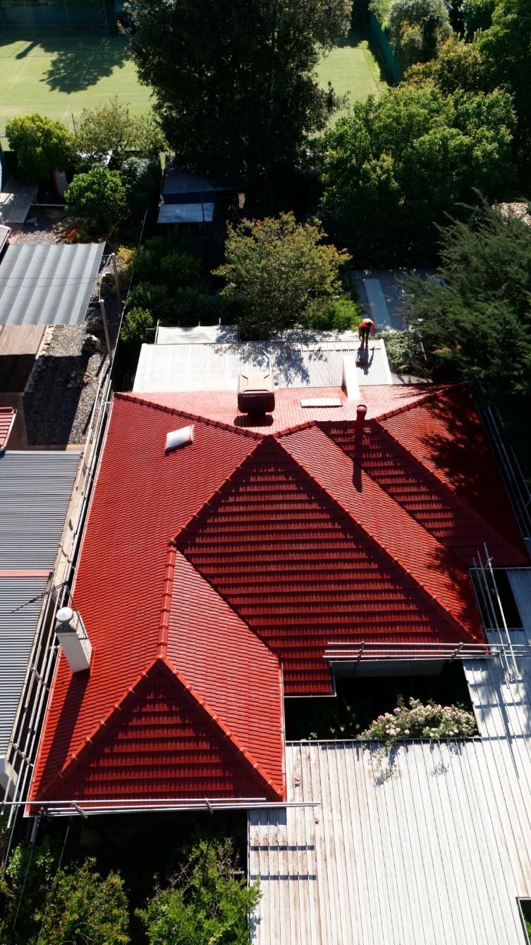 Aerial view of a red-roofed house surrounded by trees and neighboring rooftops.