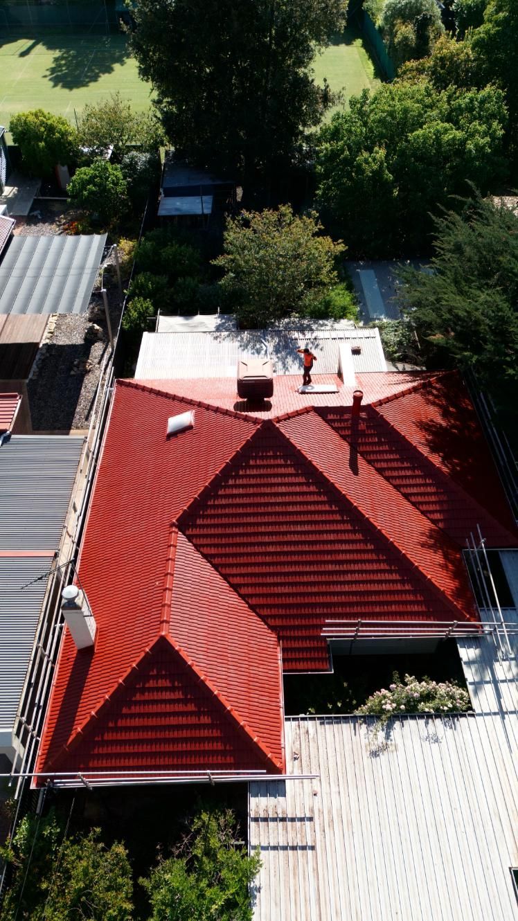 Aerial view of a red-roofed house surrounded by trees and neighboring buildings.