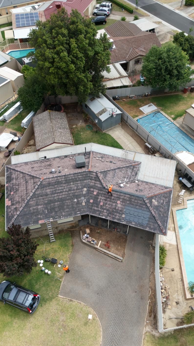 Aerial view of houses with tiled roofs, a driveway, trees, and a blue swimming pool