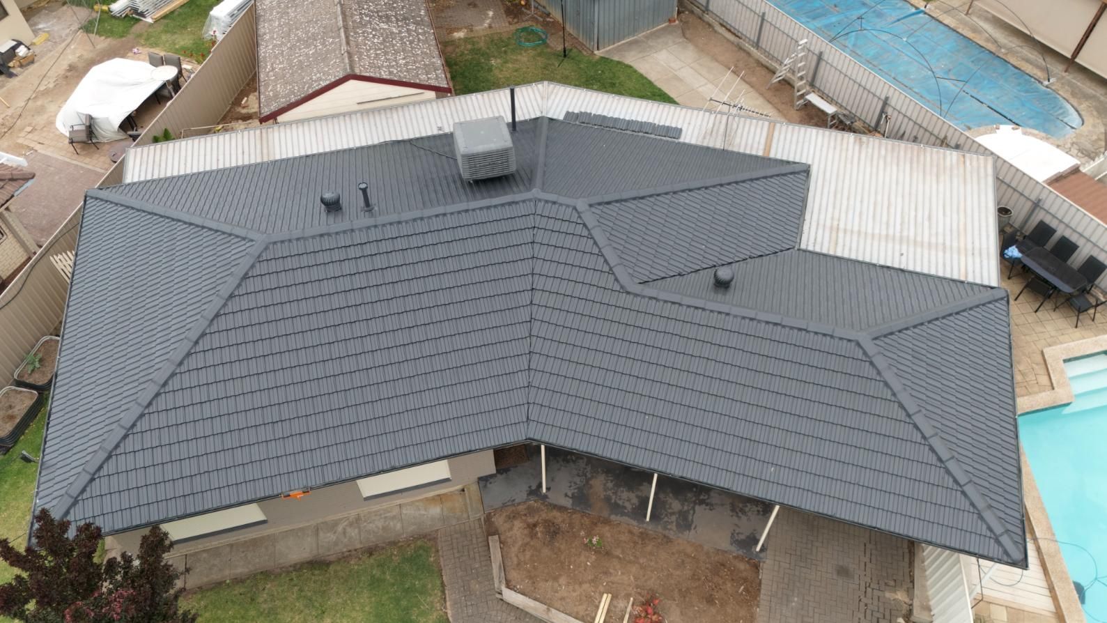 Aerial view of a gray shingle roof on a house with a backyard and swimming pool nearby.
