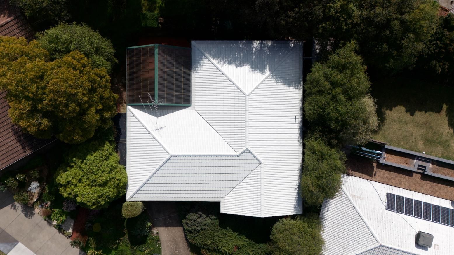 Aerial view of white-roofed houses surrounded by trees and a road.