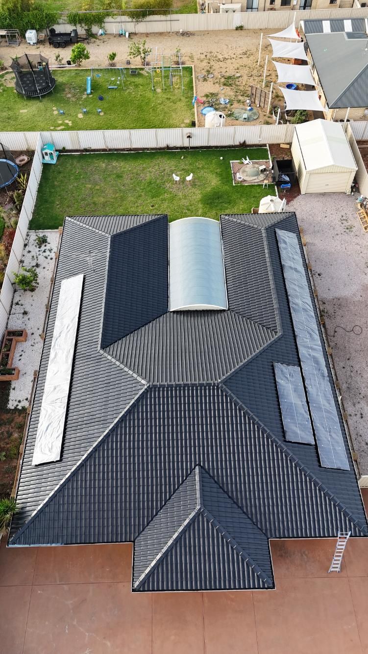 Aerial view of a house with a dark shingled roof and small yard, surrounded by neighboring homes.