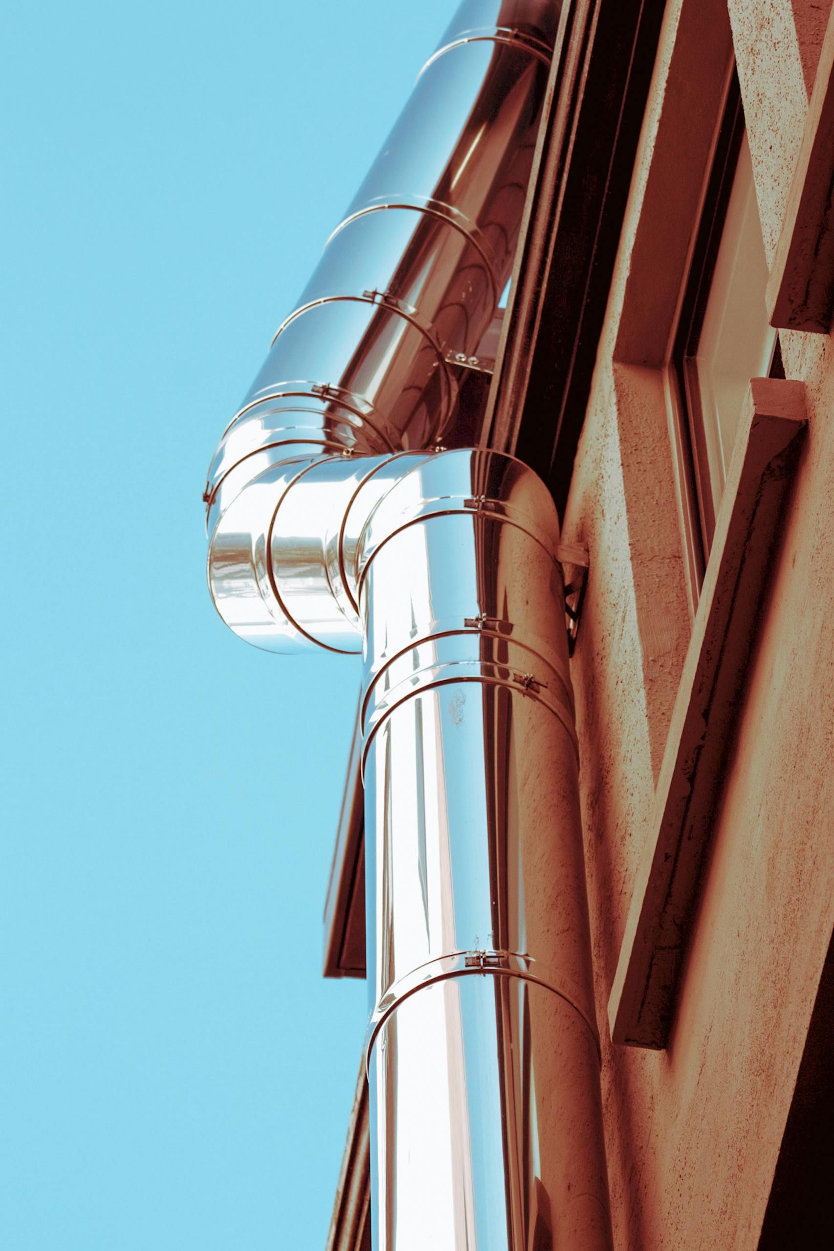 Shiny silver downspout on a red brick building against a blue sky