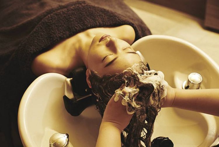 A woman is washing her hair in a sink with her eyes closed