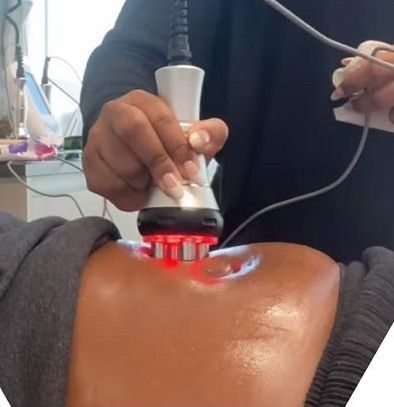 Person using a device with red lights on a person's abdomen. The person is lying down, receiving a cosmetic treatment.