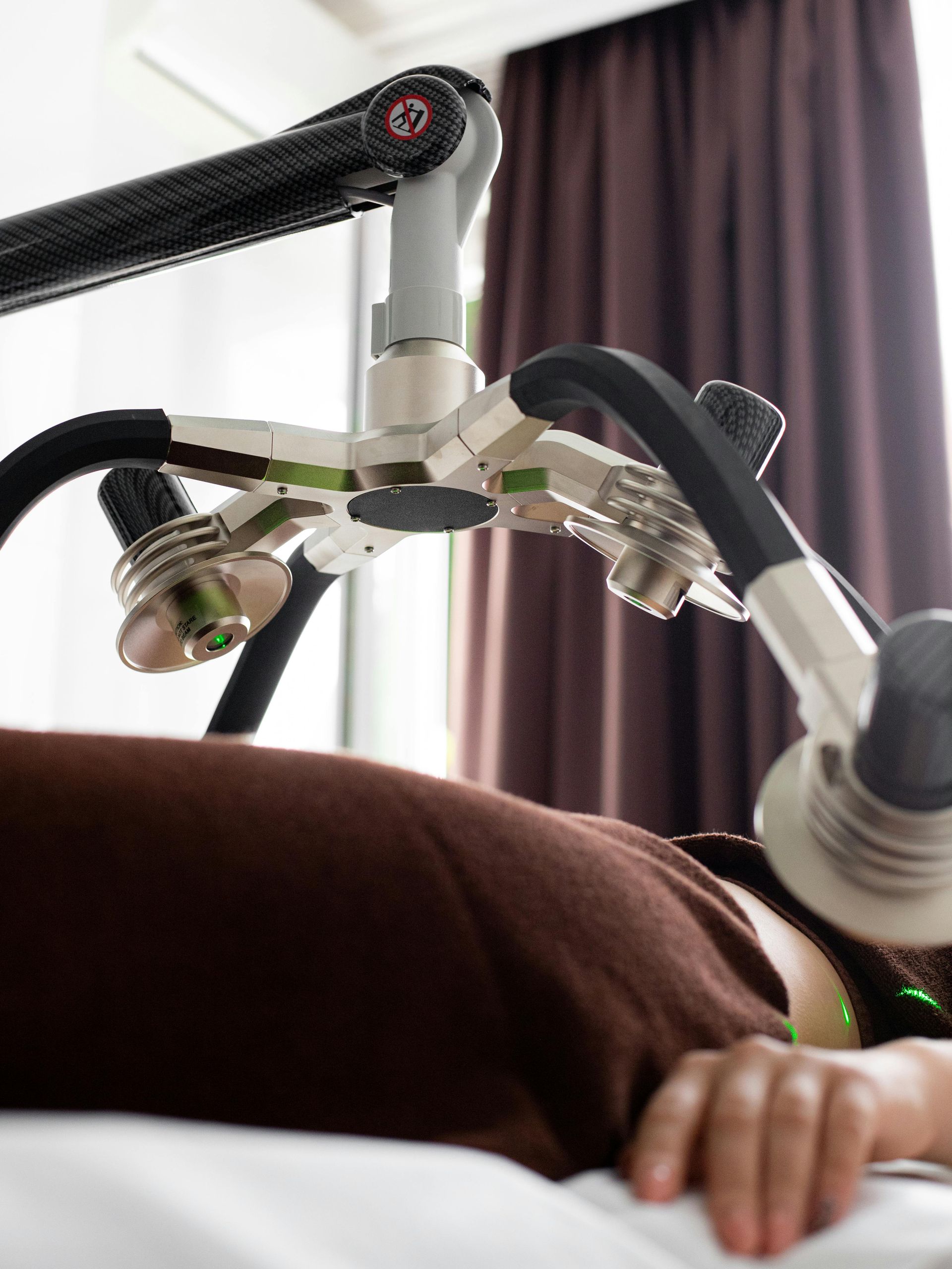 Person receiving laser therapy, lying down under an articulated arm device with multiple laser heads.