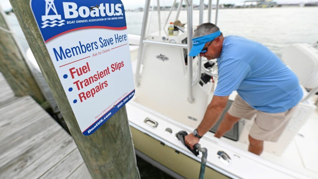 A man is pumping gas into a boat with a boatus sign in the background