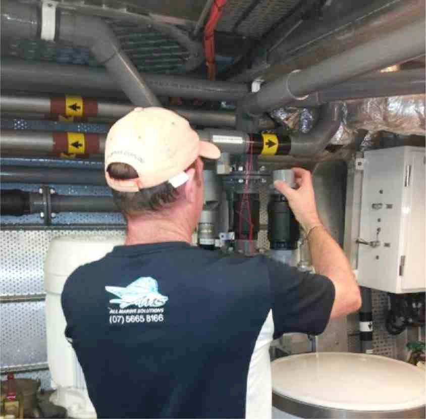A man wearing a blue shirt with a fish on the back is working on pipes