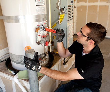 A man is working on a water heater in a garage.