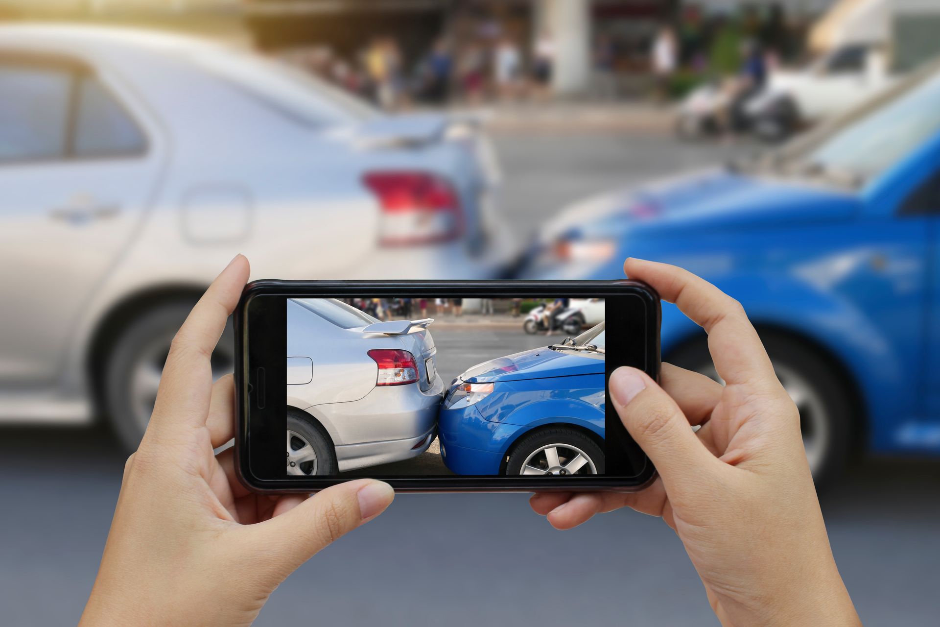 A person's hand is holding a smartphone and taking a photo of a car accident.