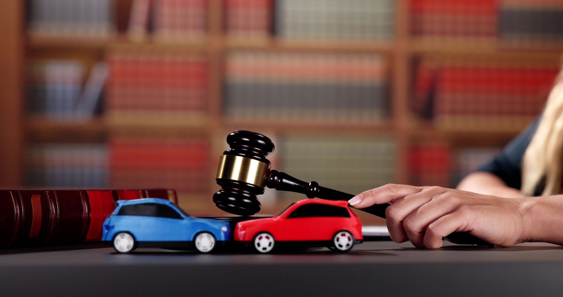 Two toy cars on a table with a lawyer with a gavel in the background.