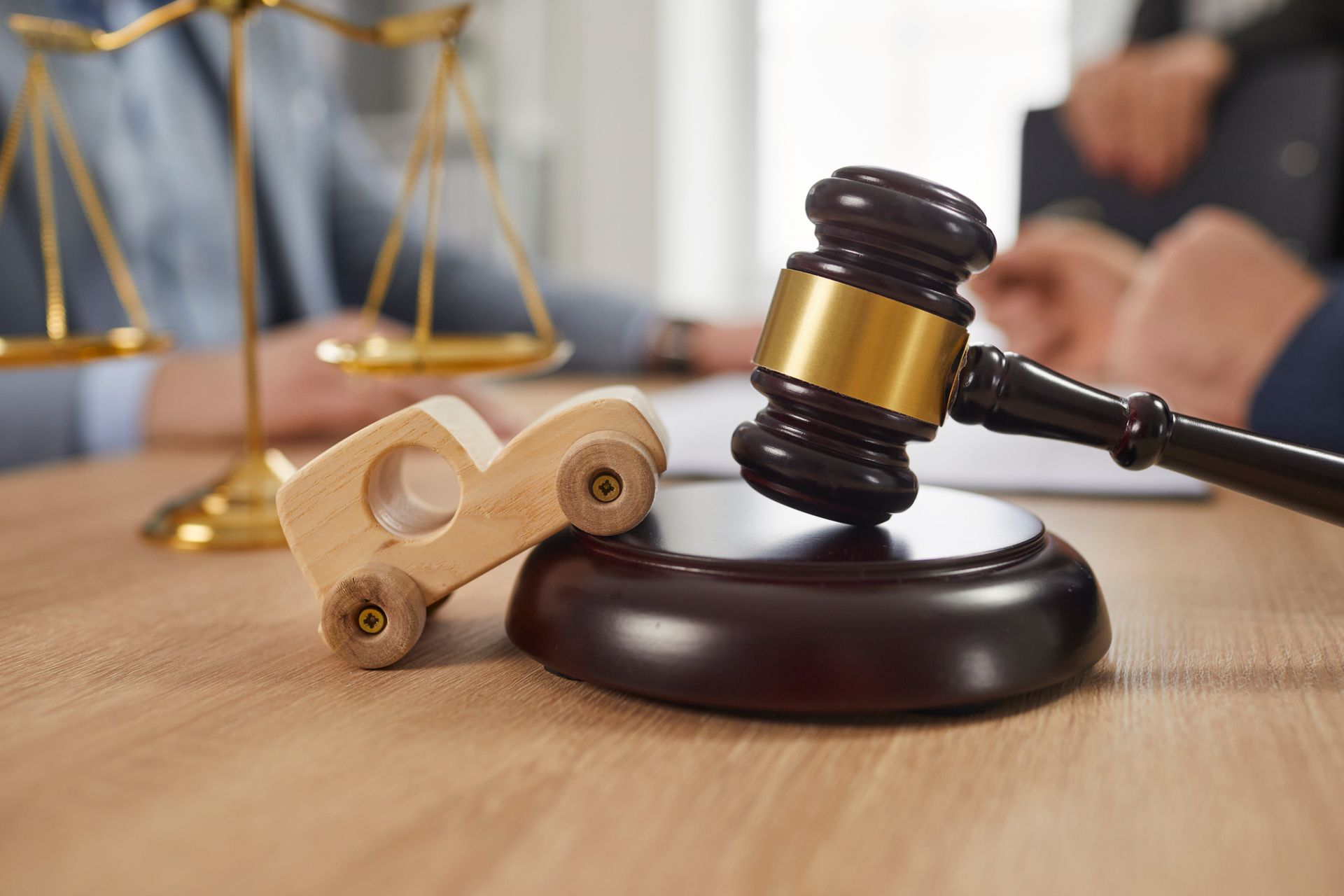 Toy car, gavel, and scales of justice on the table, with accident lawyers in the background.