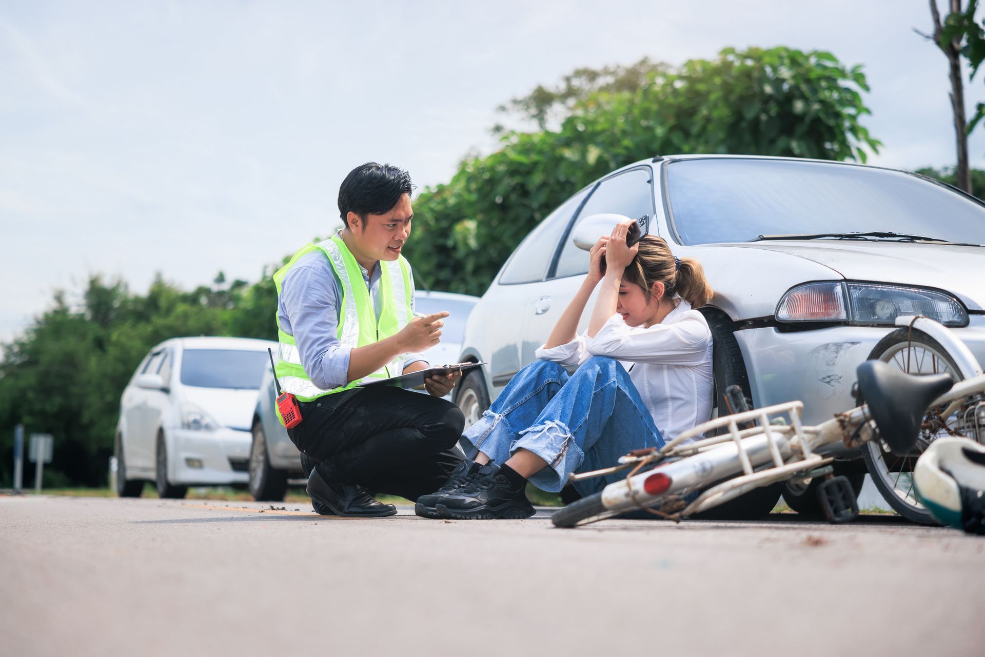 A woman is sitting next to her crashed car by a motorcycle and talking to a man.