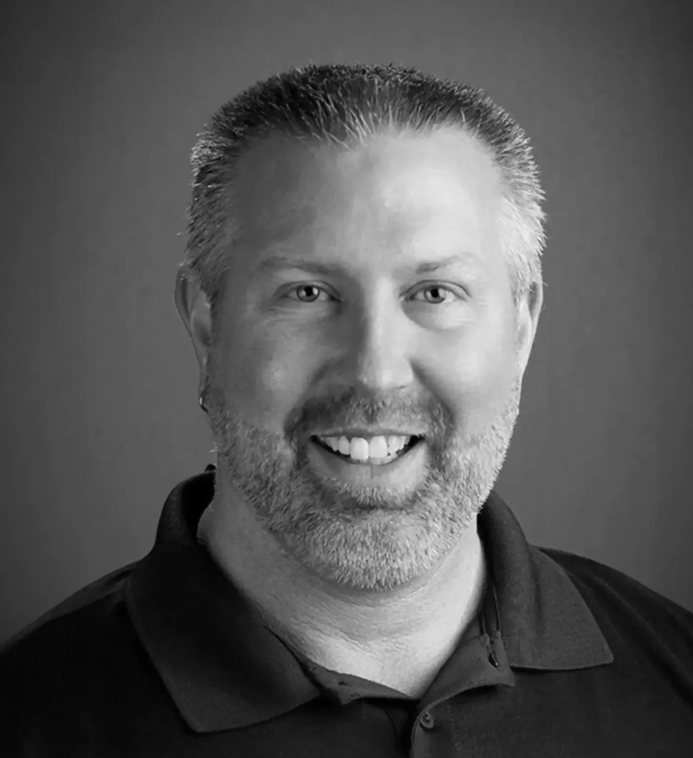 Man with a beard and short hair smiling at the camera, wearing a dark collared shirt.