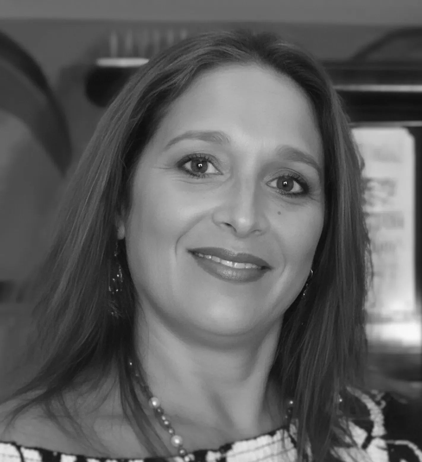 Woman with long hair smiles, wearing off-the-shoulder top, pearl necklace, and earrings.