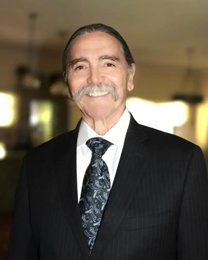 Smiling man in a suit and tie, against a blurred background.
