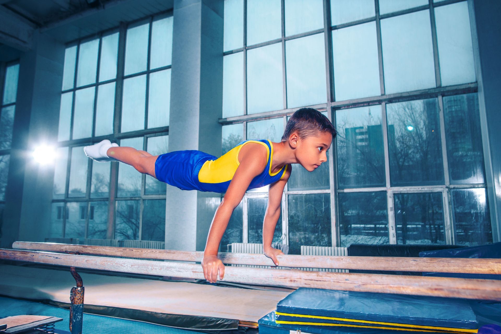 Boy in blue and yellow leotard balances on parallel bars in a gym.