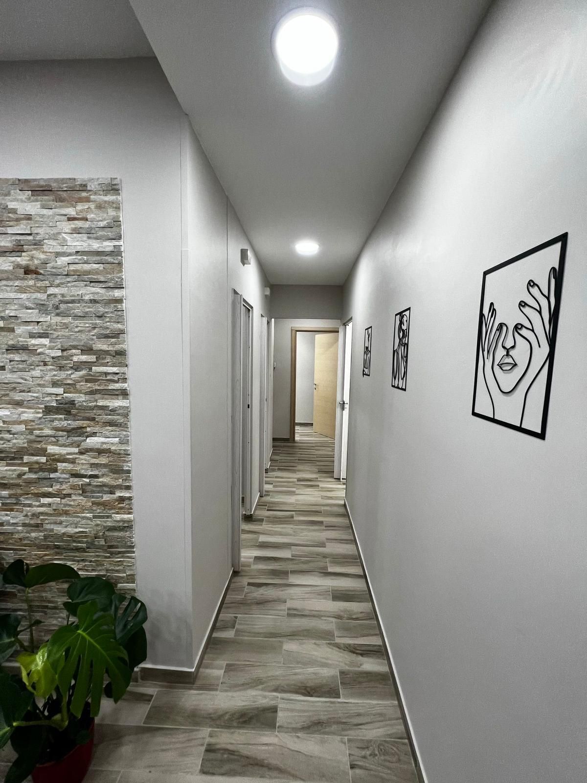 Lungo corridoio con pareti grigie, pavimento effetto legno e opere d'arte. Sulla sinistra si trova una parete con elementi in pietra e luci incassate nel soffitto.