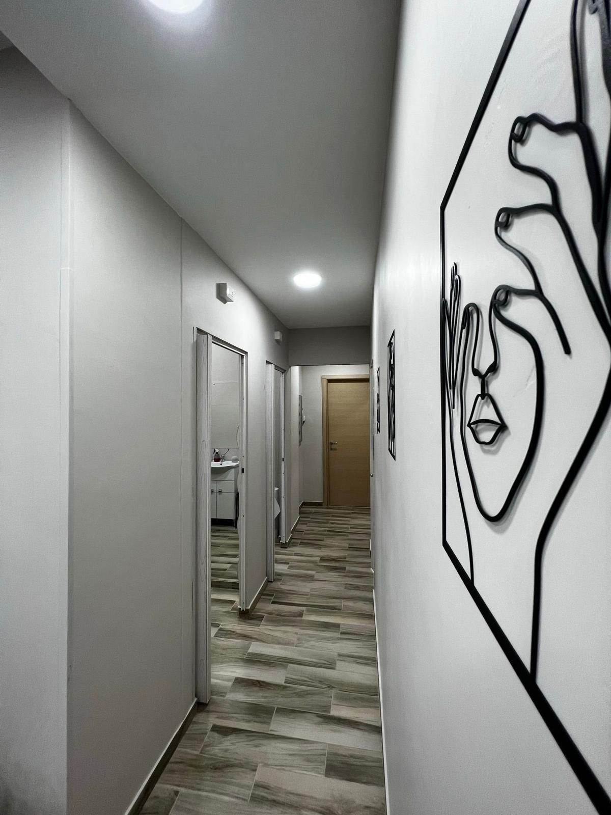 Corridoio stretto con pareti grigie, pavimento effetto legno, opere d'arte e porte.