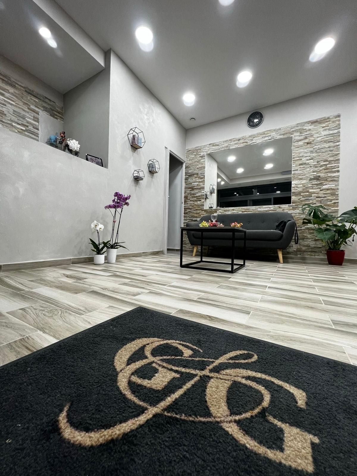 Ingresso di un salone, con zerbino con logo, divano e parete con elementi decorativi in pietra.