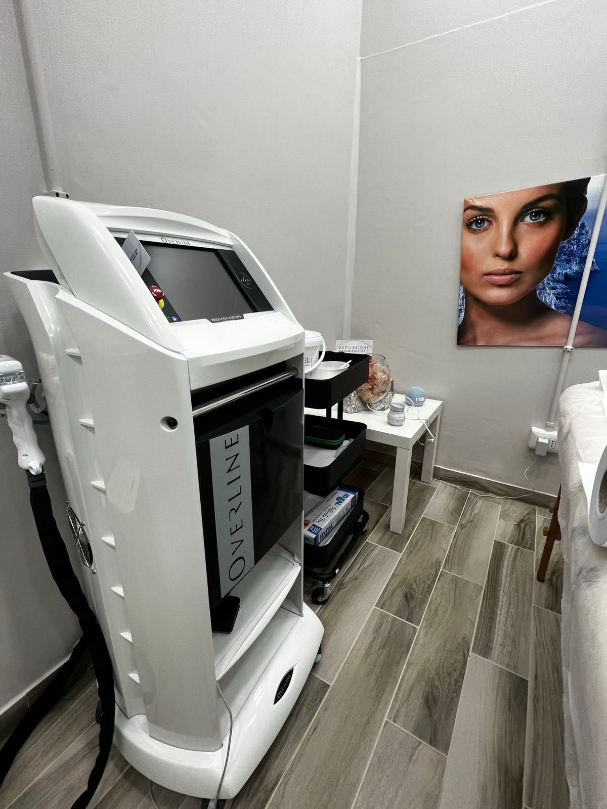 Apparecchio estetico bianco in una sala trattamenti accanto a un tavolino con materiali e un ritratto.