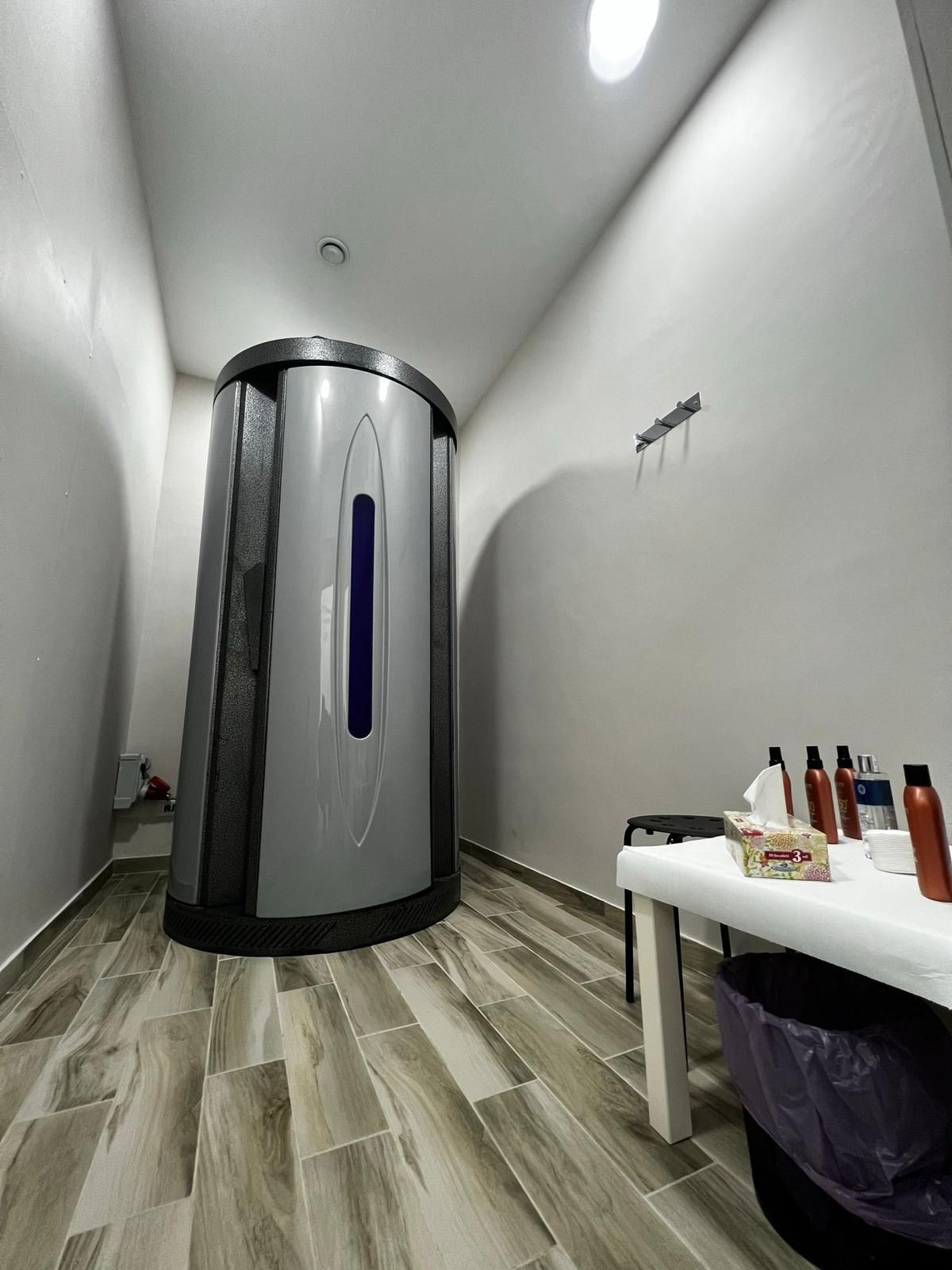 Cabina abbronzante in una piccola stanza con un tavolo con le lozioni e un sacco della spazzatura.