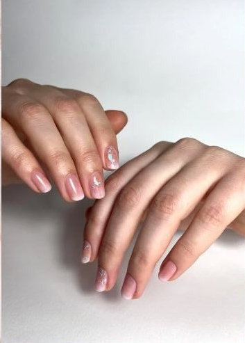 Mani con unghie curate, stile french manicure, su una superficie bianca.