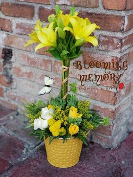 A yellow pot filled with yellow flowers and a butterfly is sitting in front of a brick wall.