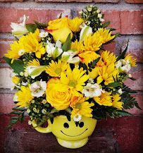A smiley face filled with yellow flowers is sitting on a brick wall.