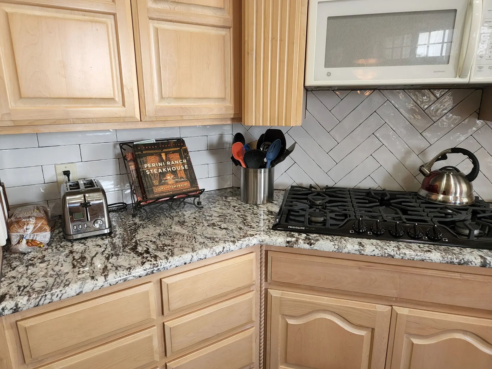 Kitchen corner with light cabinets, granite countertop, stove, and herringbone tile backsplash.