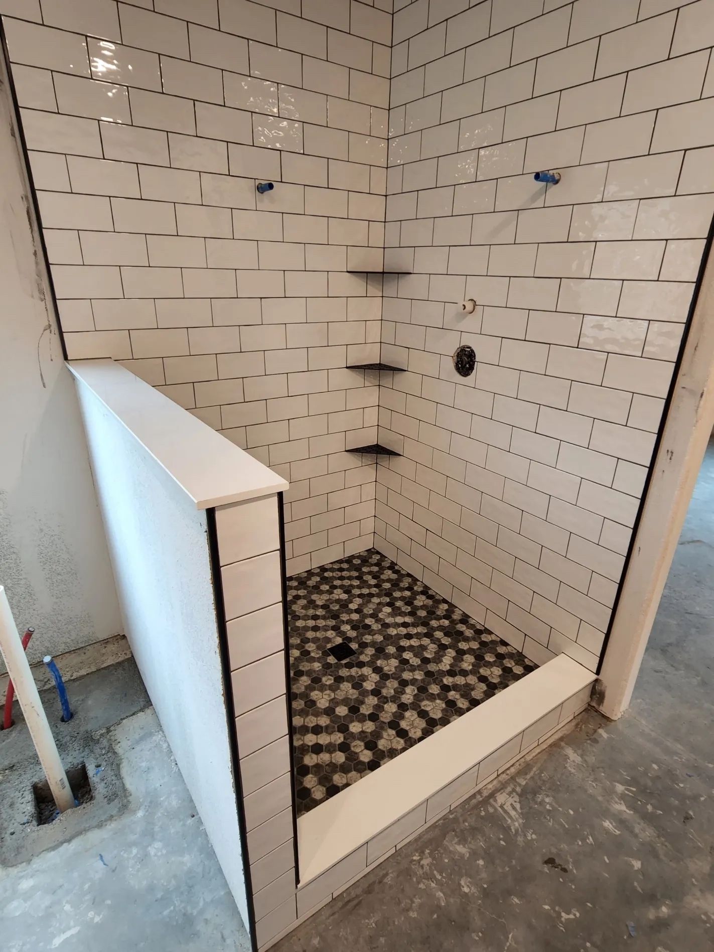 Newly tiled shower stall with white subway tiles, black grout, and pebble floor.