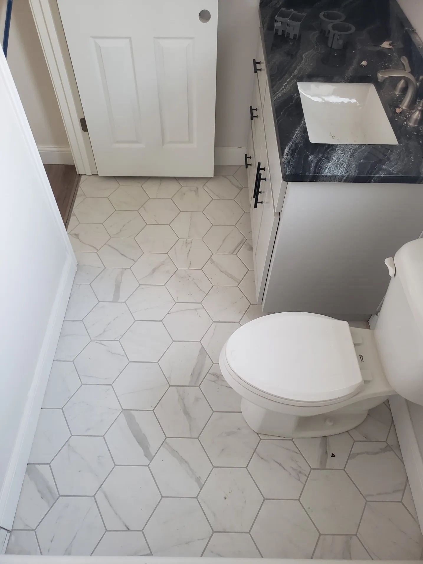 Bathroom with white hexagon tile floor, white toilet, vanity, and door.