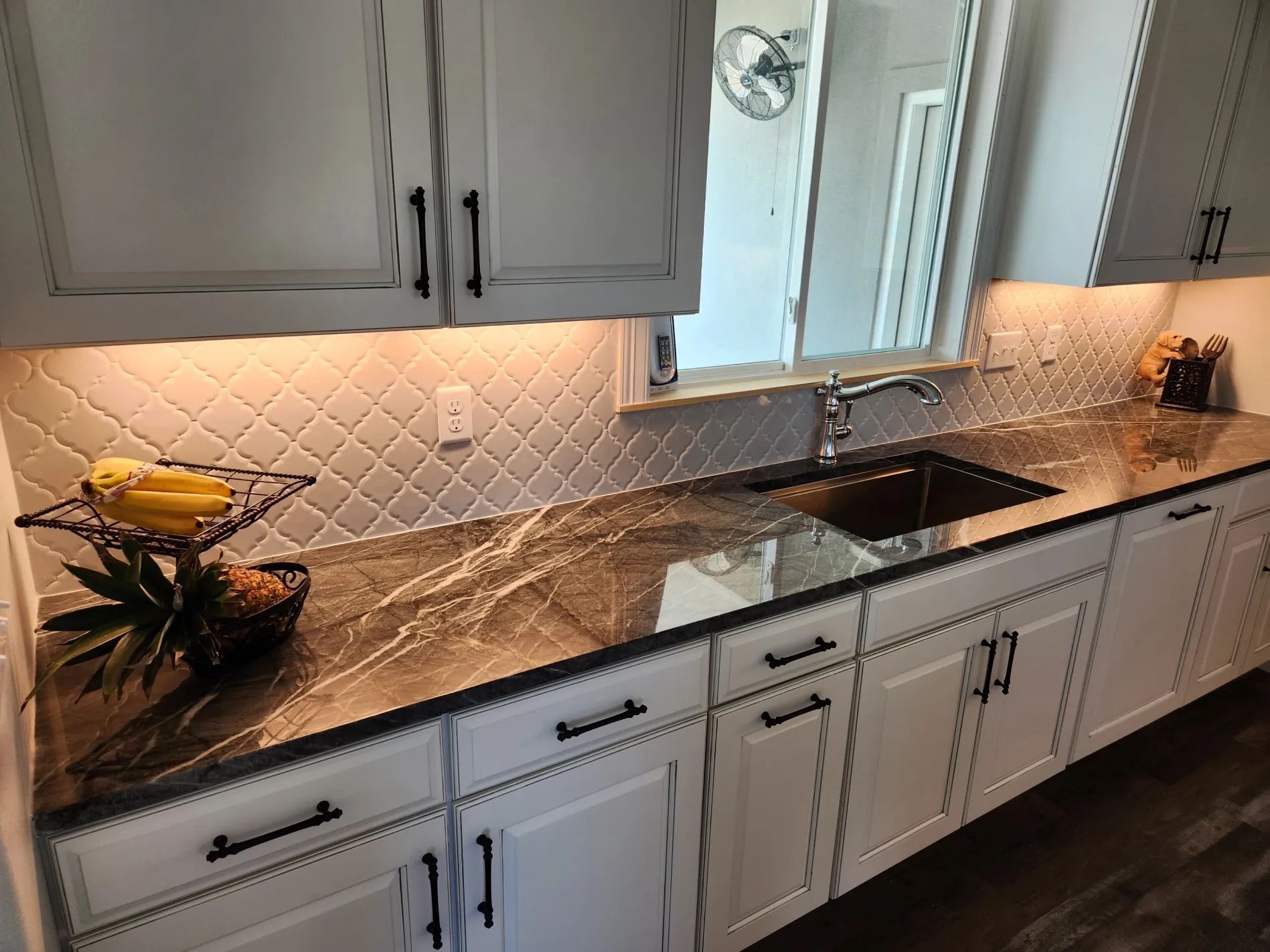 White kitchen cabinets with black hardware and a dark countertop.