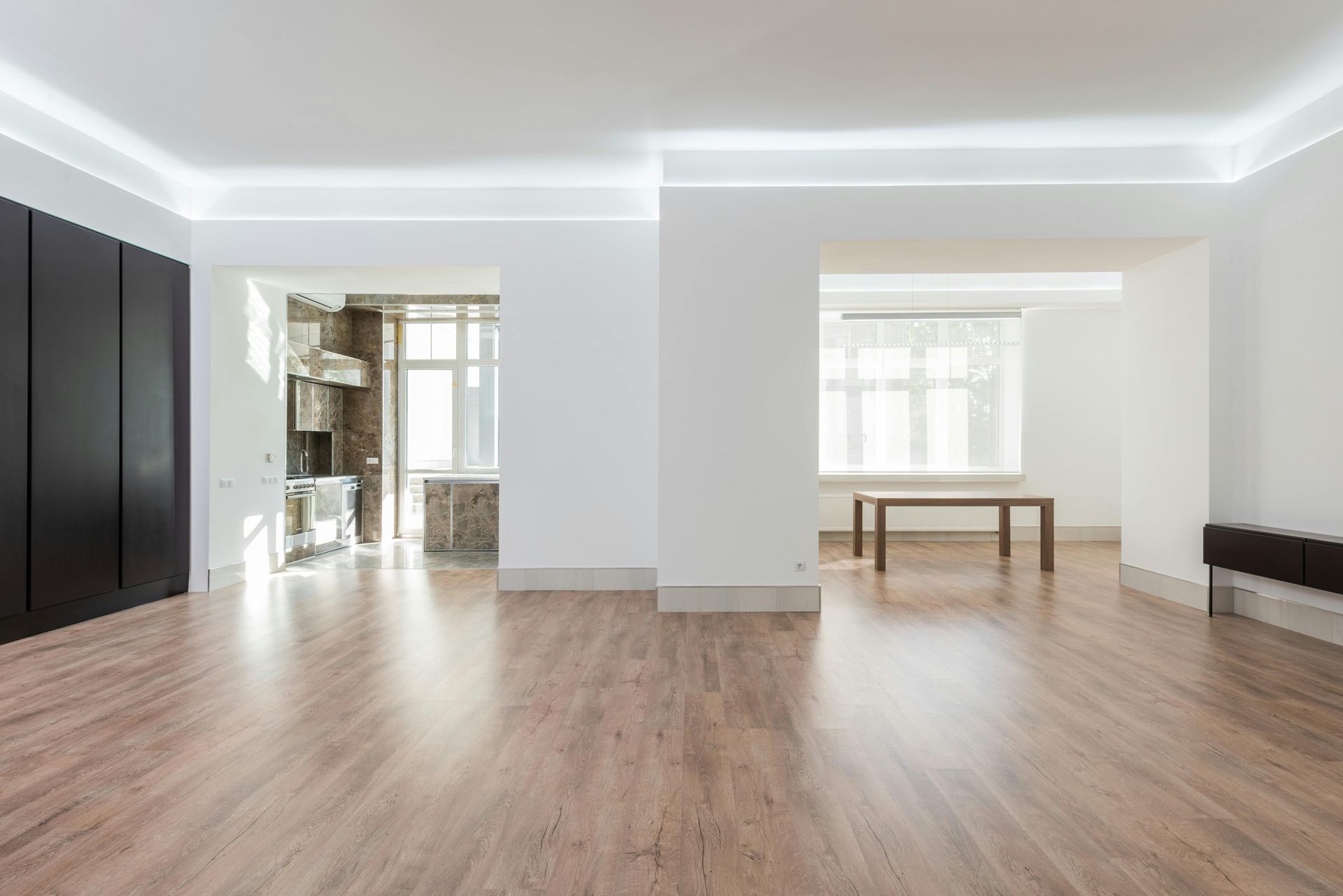 Bright, empty modern living room with wood floors, white walls, and large windows.
